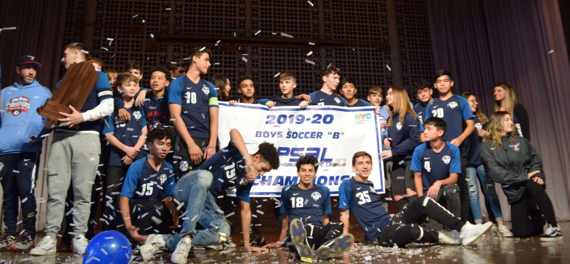 Soccer team celebrating with a championship banner on stage, surrounded by confetti.