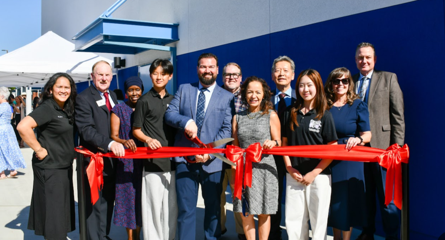 A group of people cutting a red ribbon at a celebratory event.