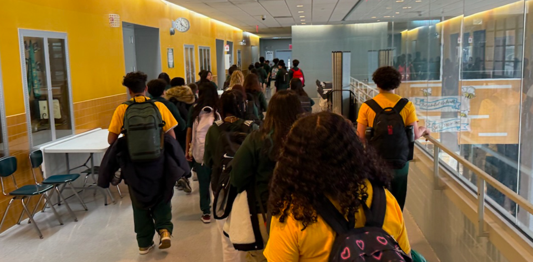 Students walking through a school corridor lined with yellow walls.