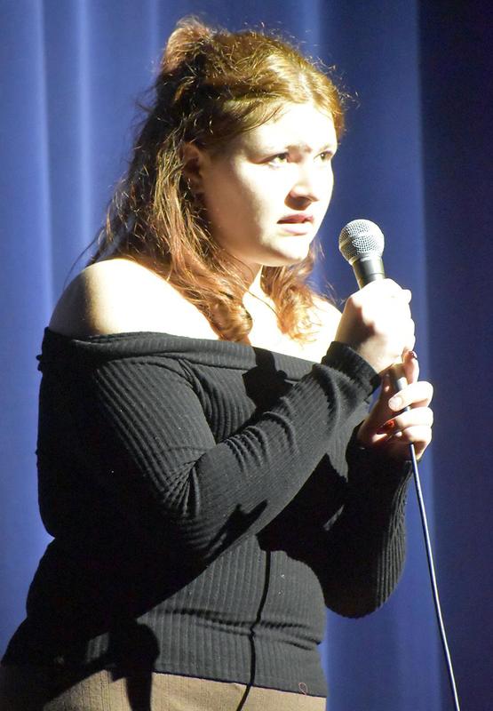 Solo performer singing into a microphone under spotlight.
