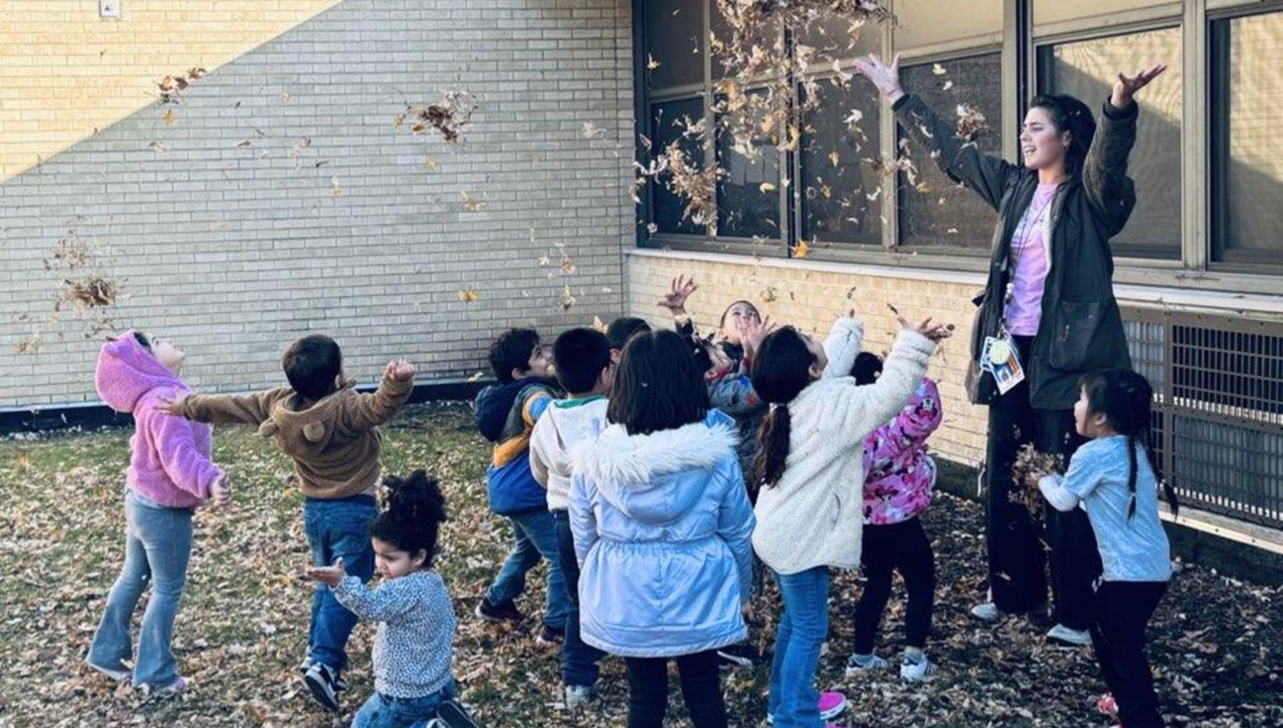 Children joyfully throwing leaves into the air outdoors under bright sunlight.