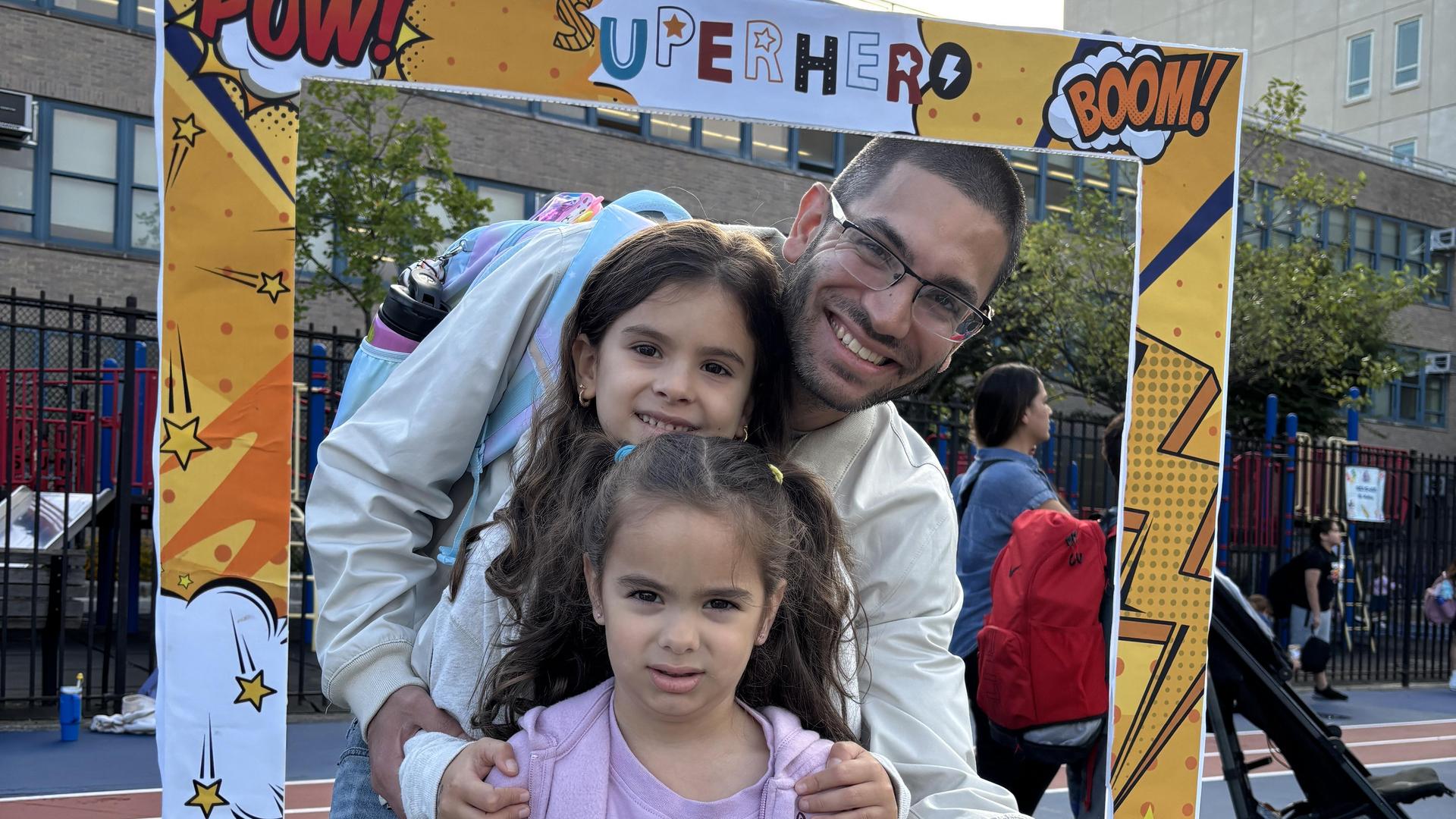 A man smiling with two children outdoors at a playground, framed by colorful graphics.