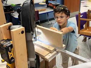 A second grade boy uses a saw to cut a piece of metal for his menorah