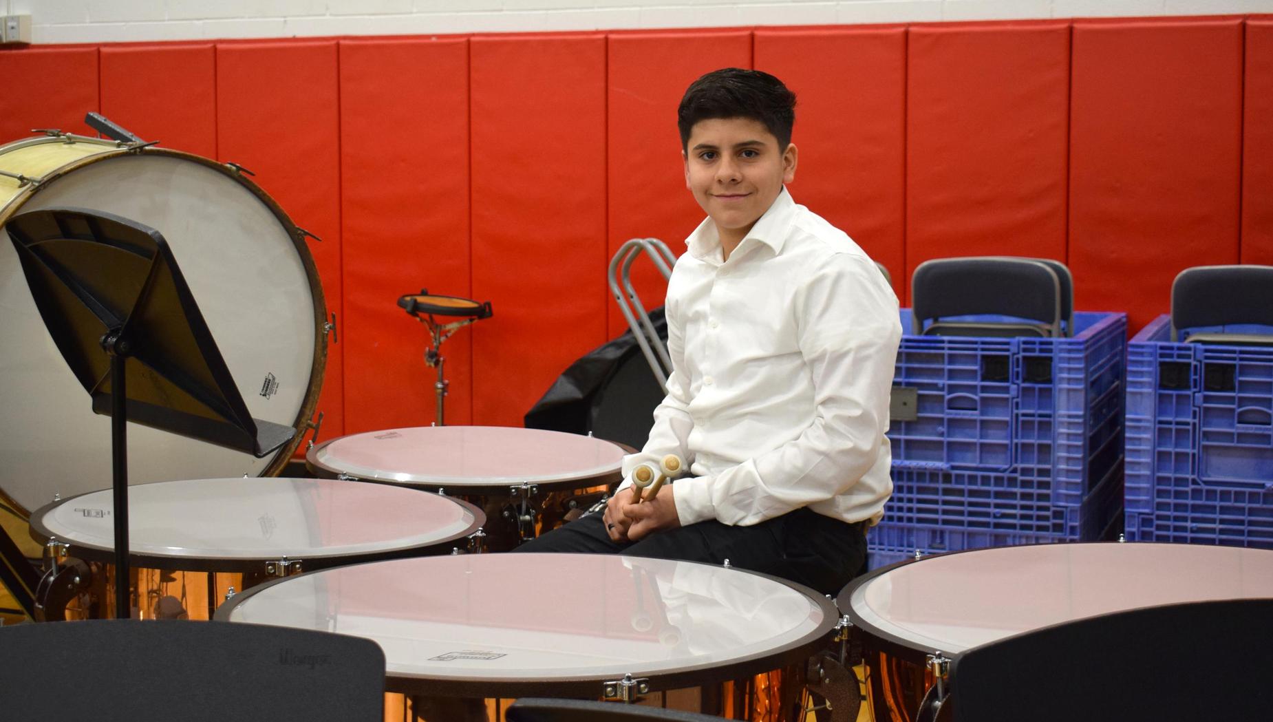 Drummer smiling while sitting at a set of timpani drums during practice.