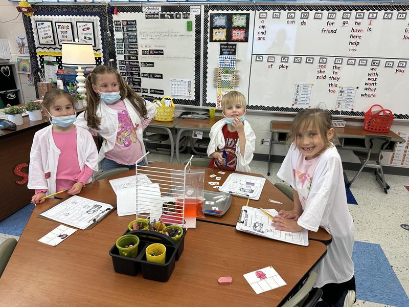 four students dressed as doctors working on vowel surgery on table