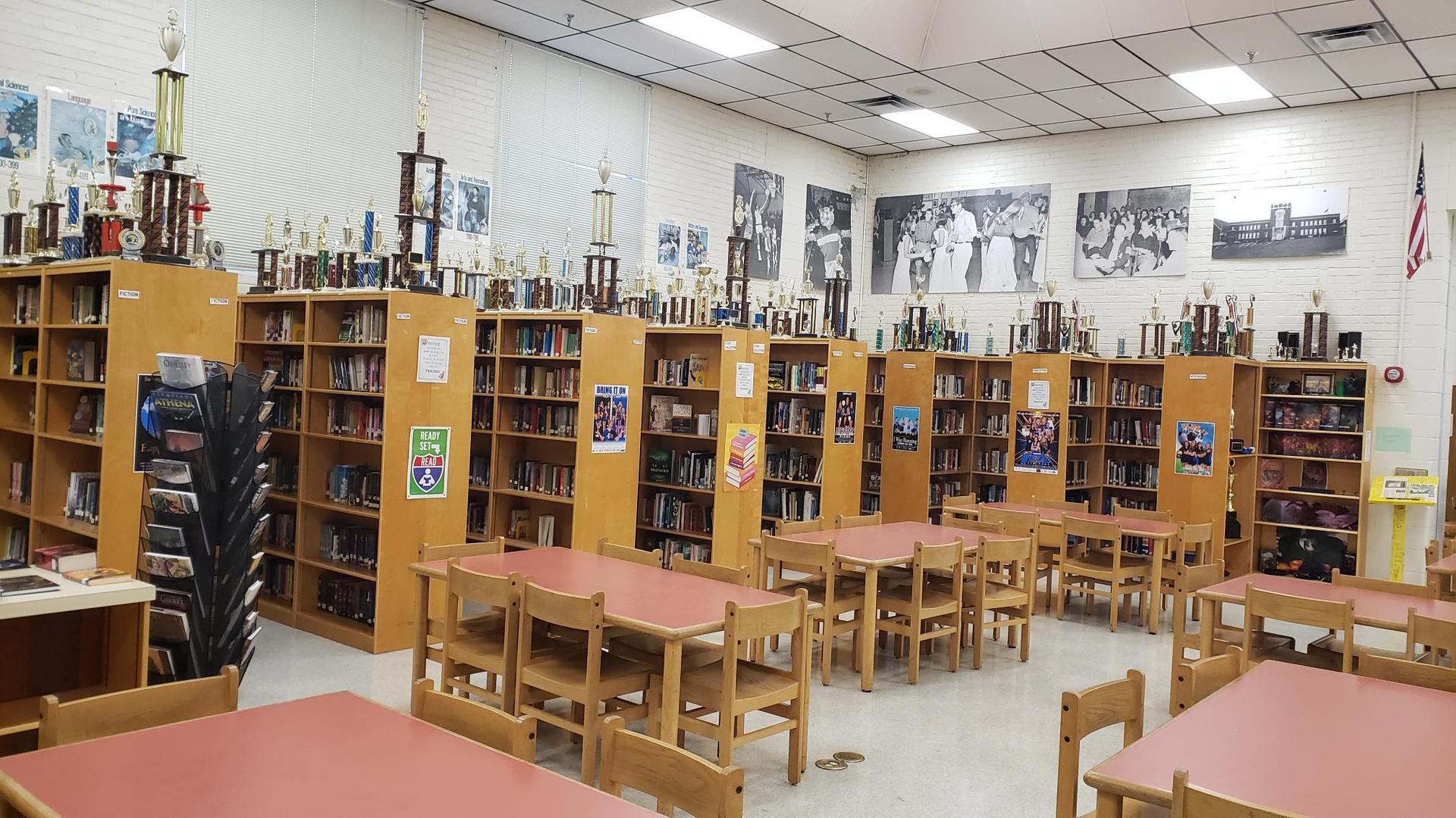Wide angle photo of SHS Library tables, chairs, bookshelves, books, and band trophies displayed