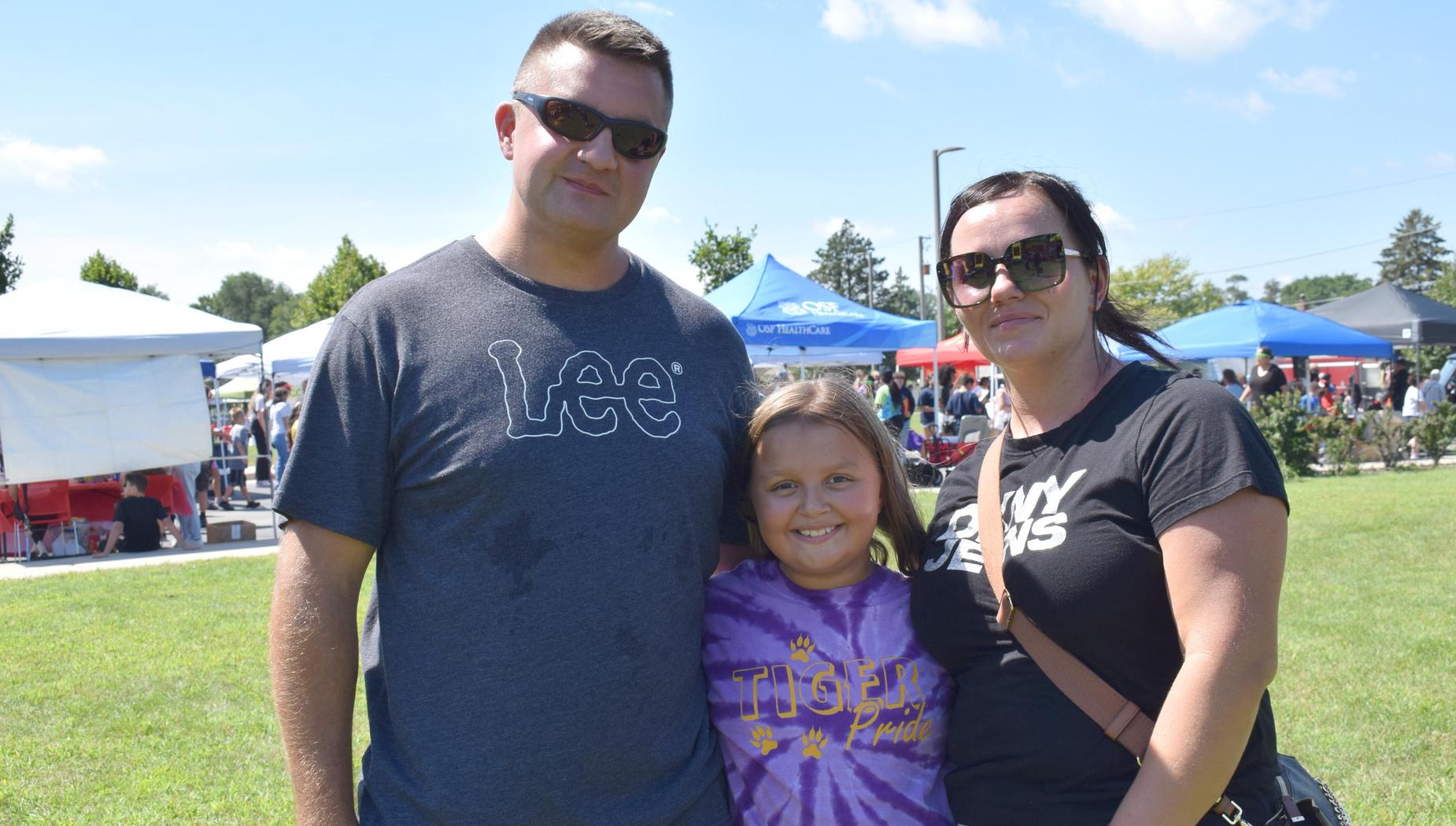 Family posing together outdoors on a sunny day at a community event.