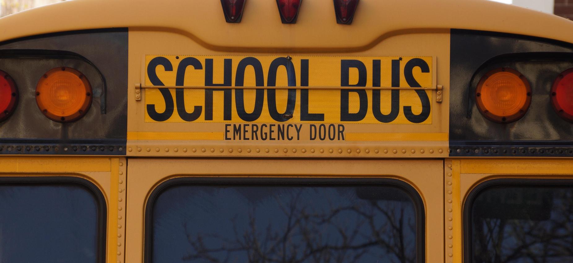 Back view of a yellow school bus with an emergency door sign.