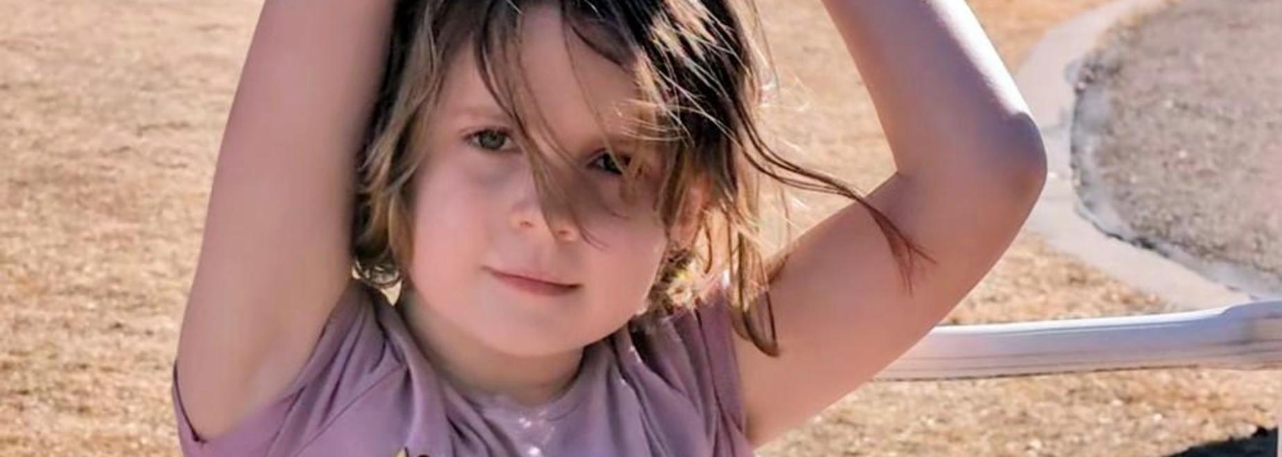 Smiling girl in a pink shirt with smiley faces posing outdoors.
