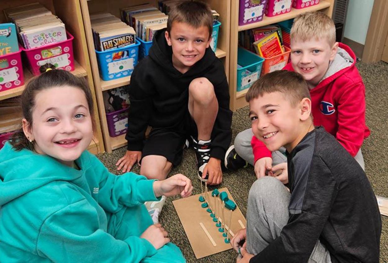 4 third-graders sit on the floor together while building a clay model in science class