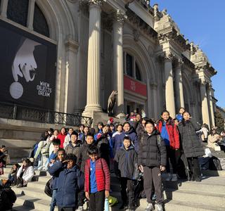 A group of students in winter coats poses on the steps of a large museum building.