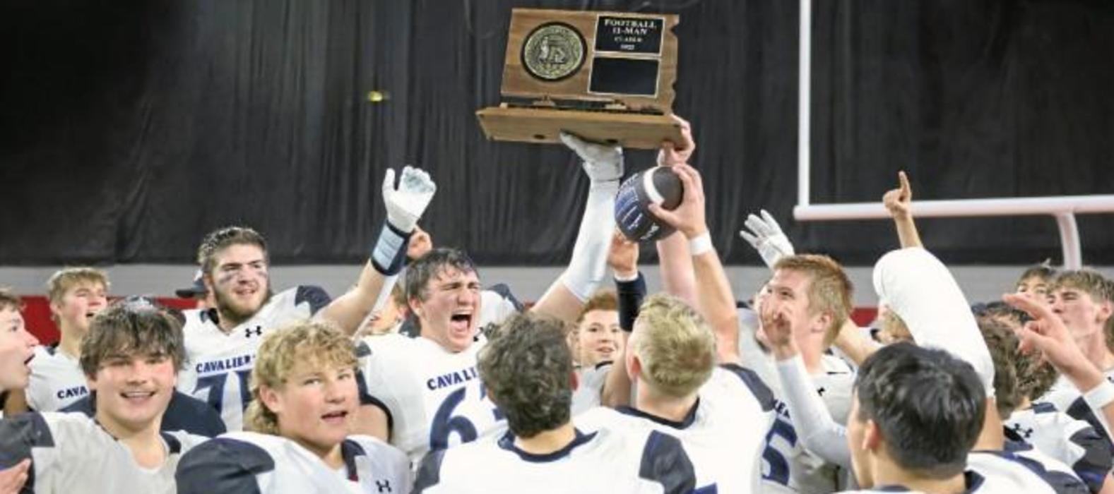 A group of excited athletes celebrate while holding a championship trophy.