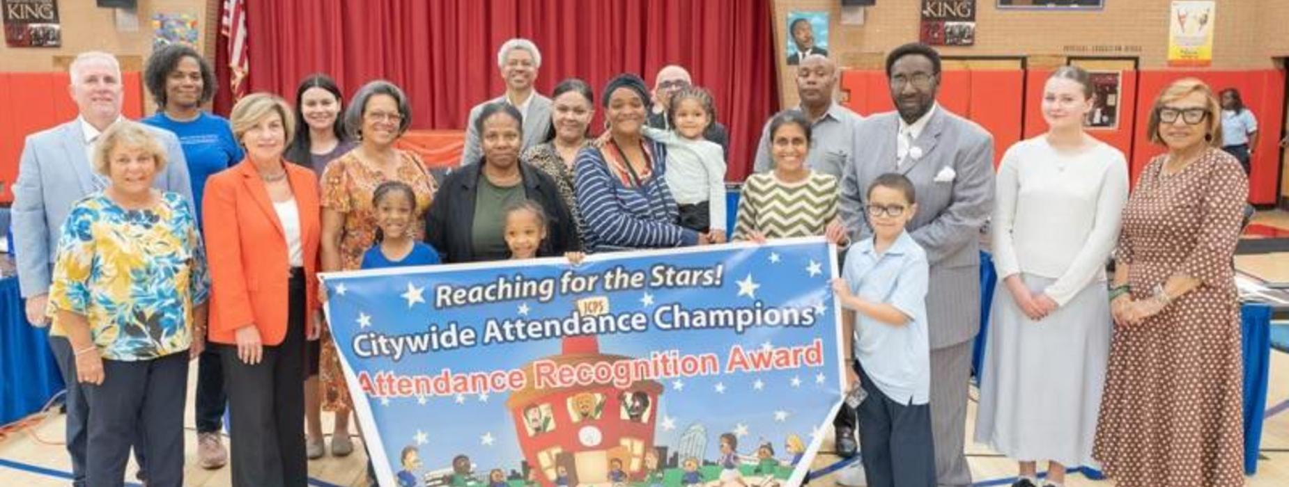 Group of people posing with an attendance recognition banner in a gymnasium.