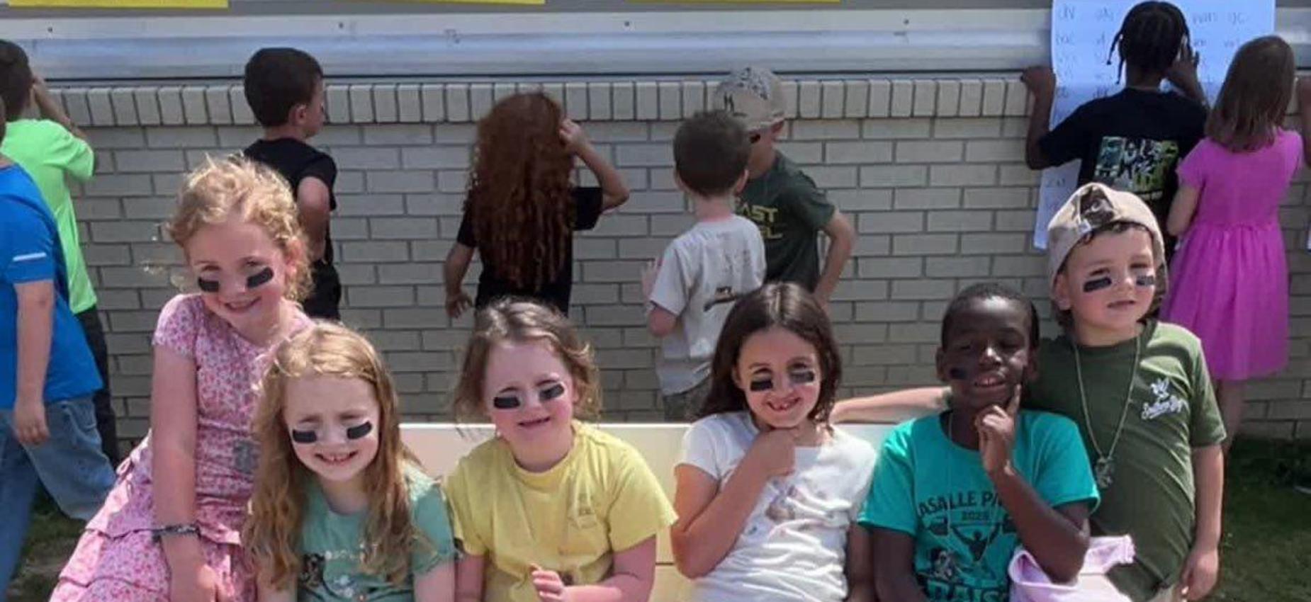 Group of children sitting on a bench outdoors, smiling and enjoying their time.