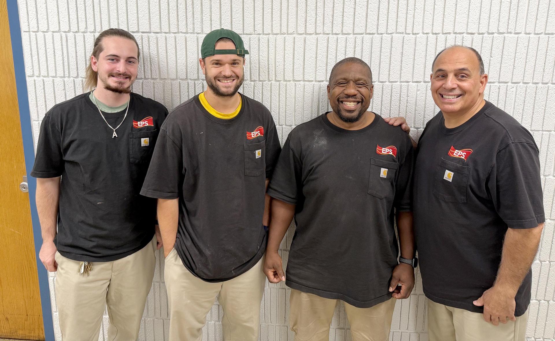 Four smiling individuals standing together, wearing matching black shirts.