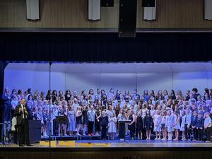 students performing in auditorium with director speaking at microphone