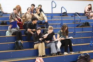 Students sit on the bleachers studying their budget worksheets at the Reality Fair