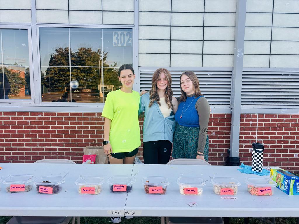 Three students from the Key Club standing behind a table of treats for a picnic.