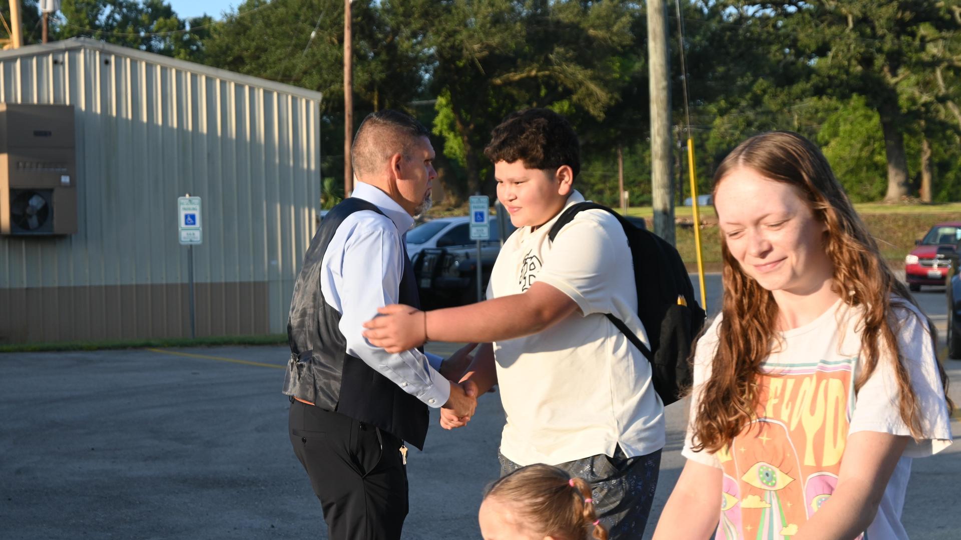 A man in a suit shakes hands with a boy, while two girls smile in the background.