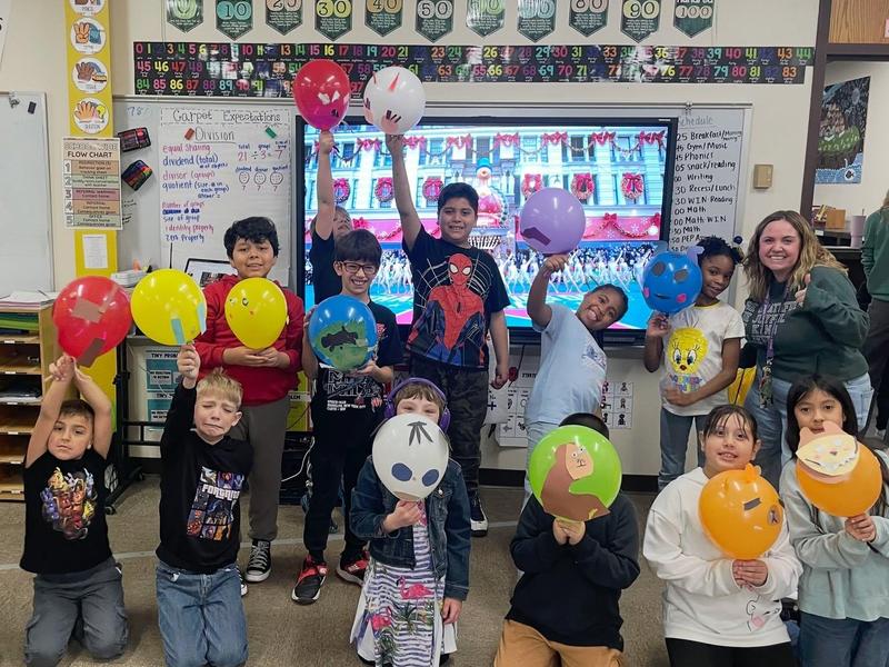 A group of children and an adult hold balloons in a classroom.