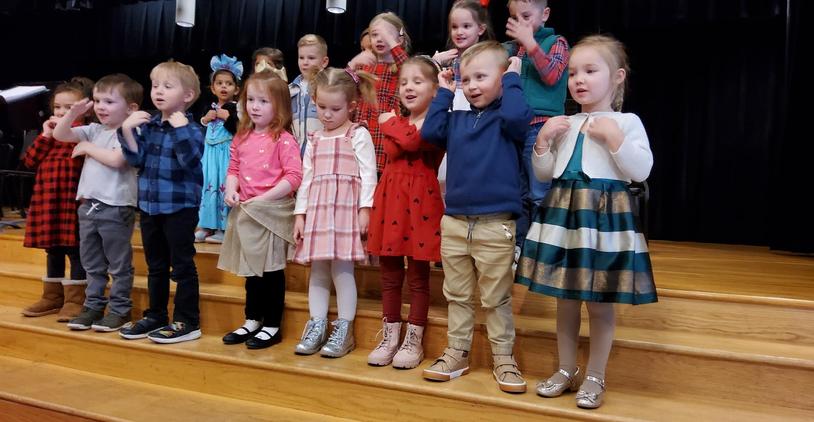 Children singing on stage in colorful outfits during a performance.