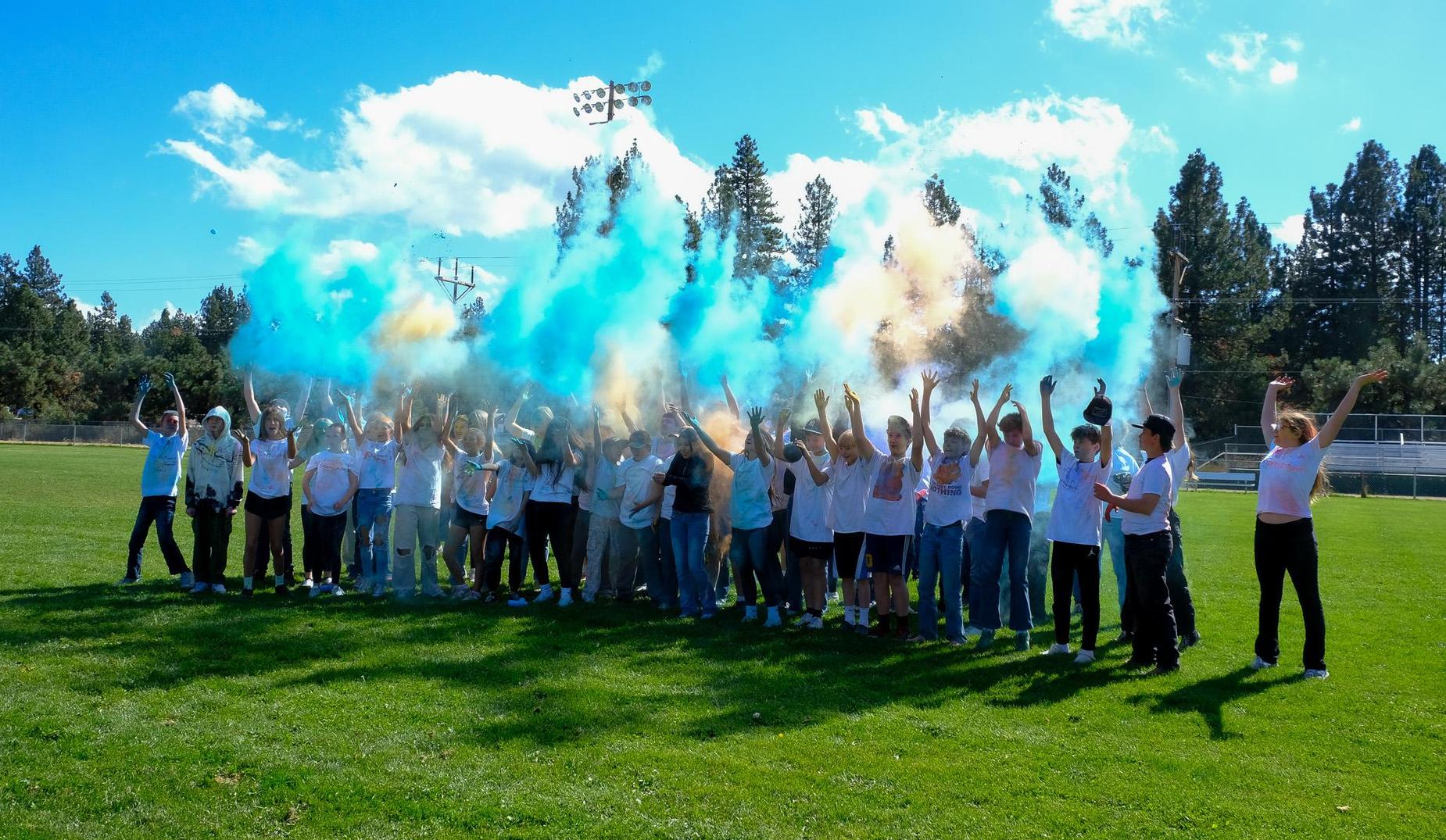 Student throw colored chalk in the air on the football field at the end of a Color Run event.
