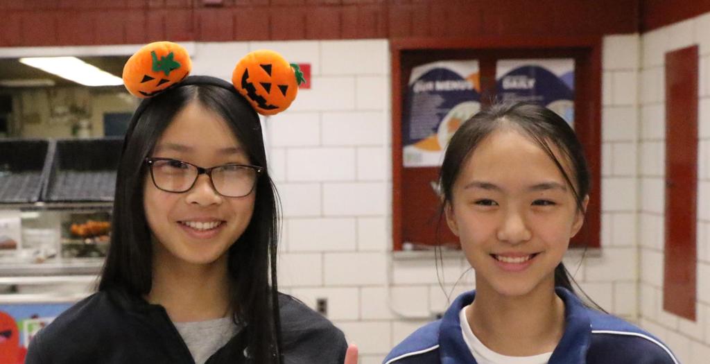 1 Girl wearing pumpkins on a headband and flashing a peace sign.