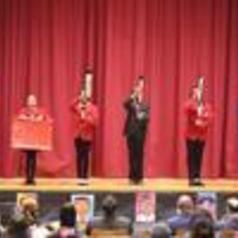 Four performers in red and black outfits on stage with a red curtain backdrop.