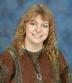 Blonde headed woman standing in front of a bush.