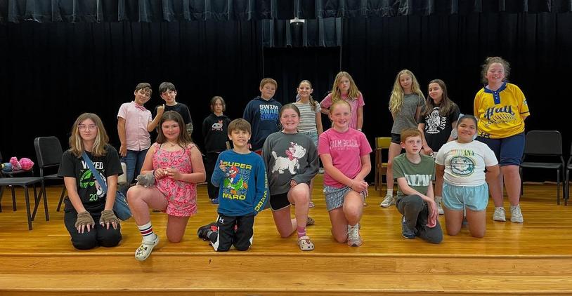 Youth performing arts group posing together in a school auditorium.
