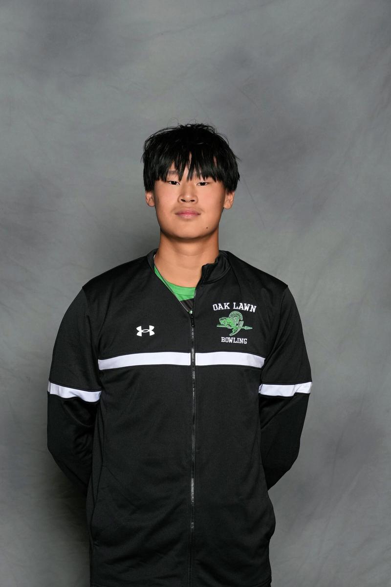 male athlete stands in front of grey backdrop with hands behind his back