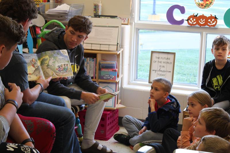 three football players read book while students look on