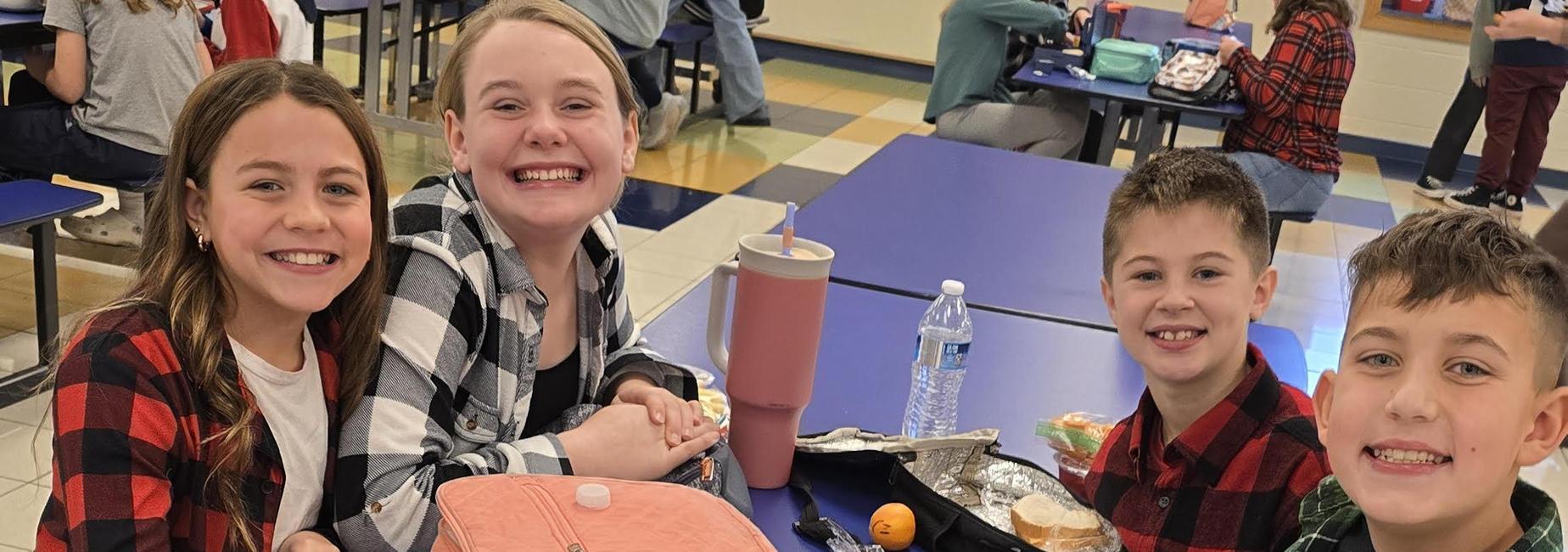 Four smiling students sitting in cafeteria with plaid shirts