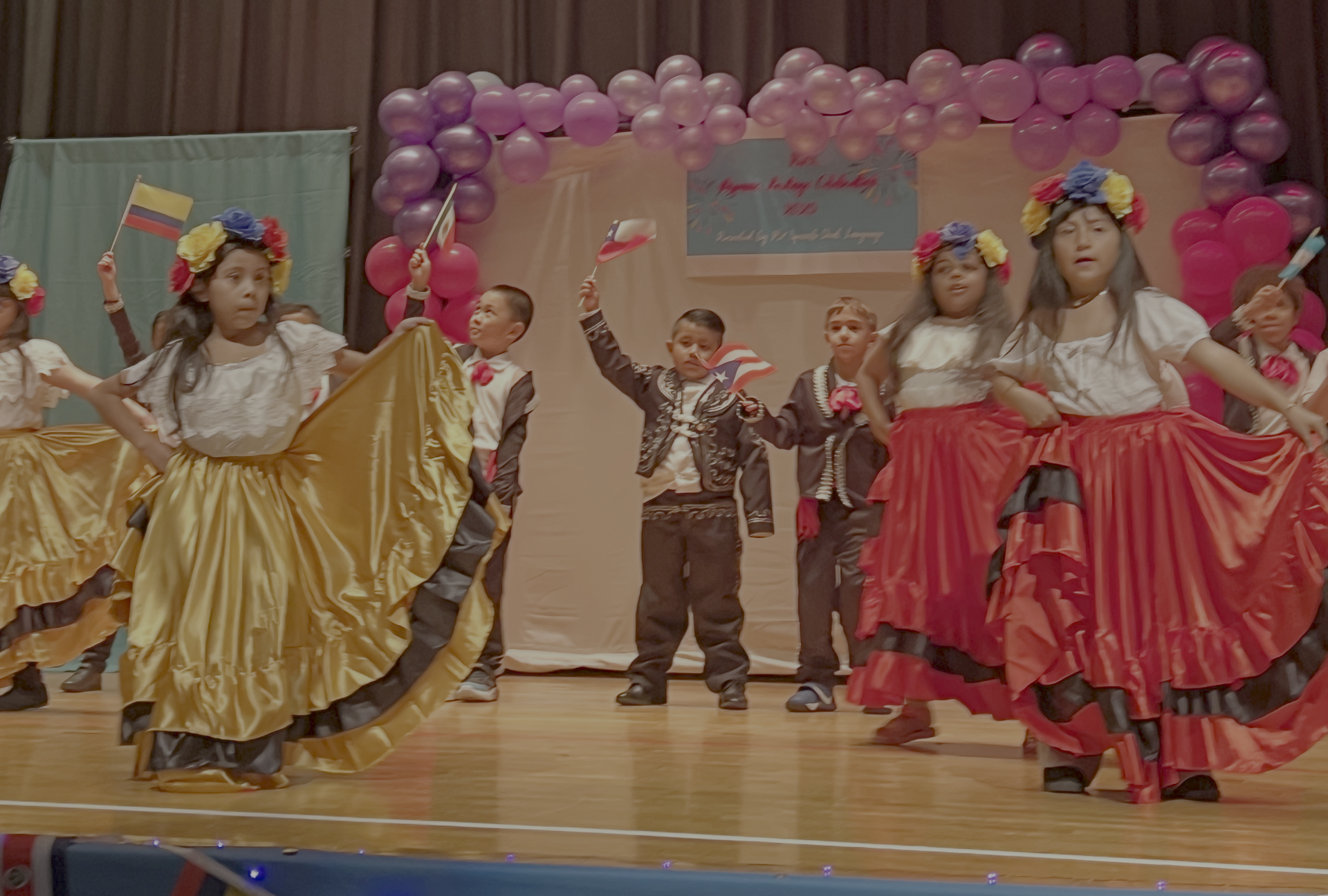 Students dressed in traditional Hispanic clothing performing a dance on stage