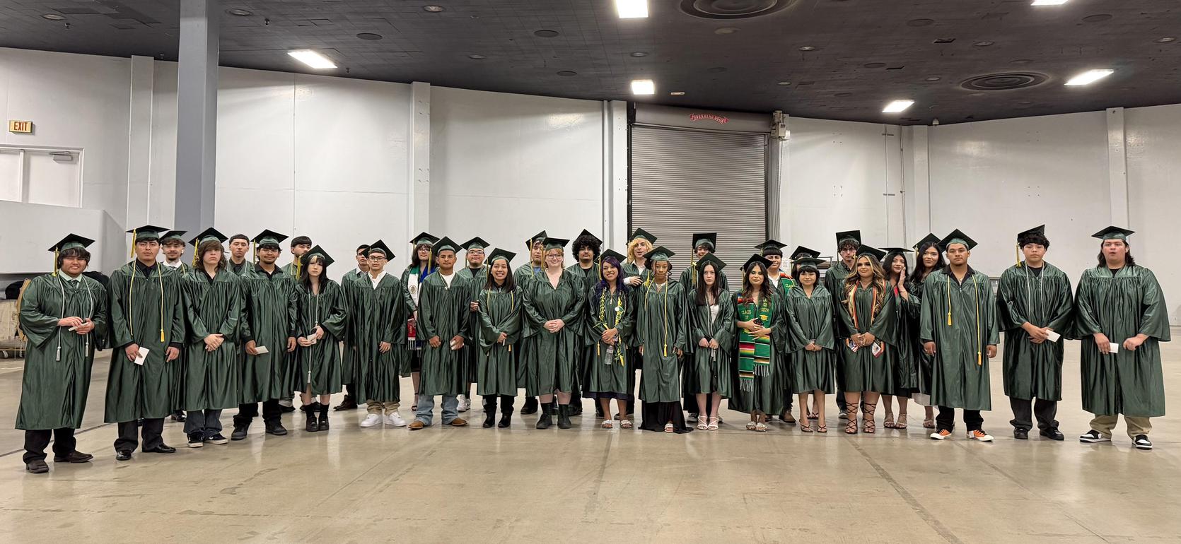 Group of graduates in green gowns and caps posing together indoors.