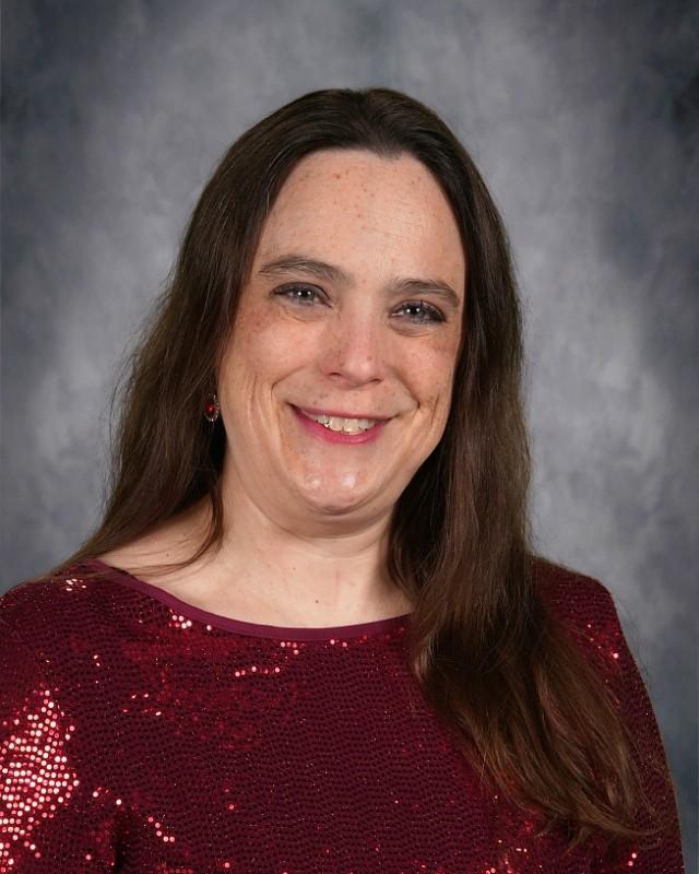 Smiling woman with long hair in a red shirt against a gray background.