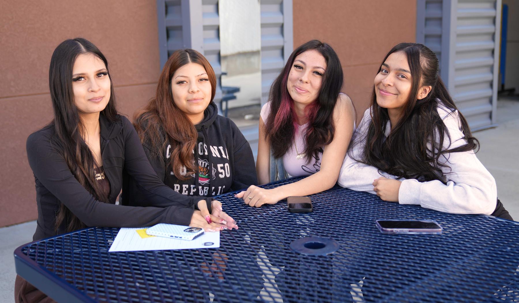 four girls sitting at a picnic table outdoors in front of school building