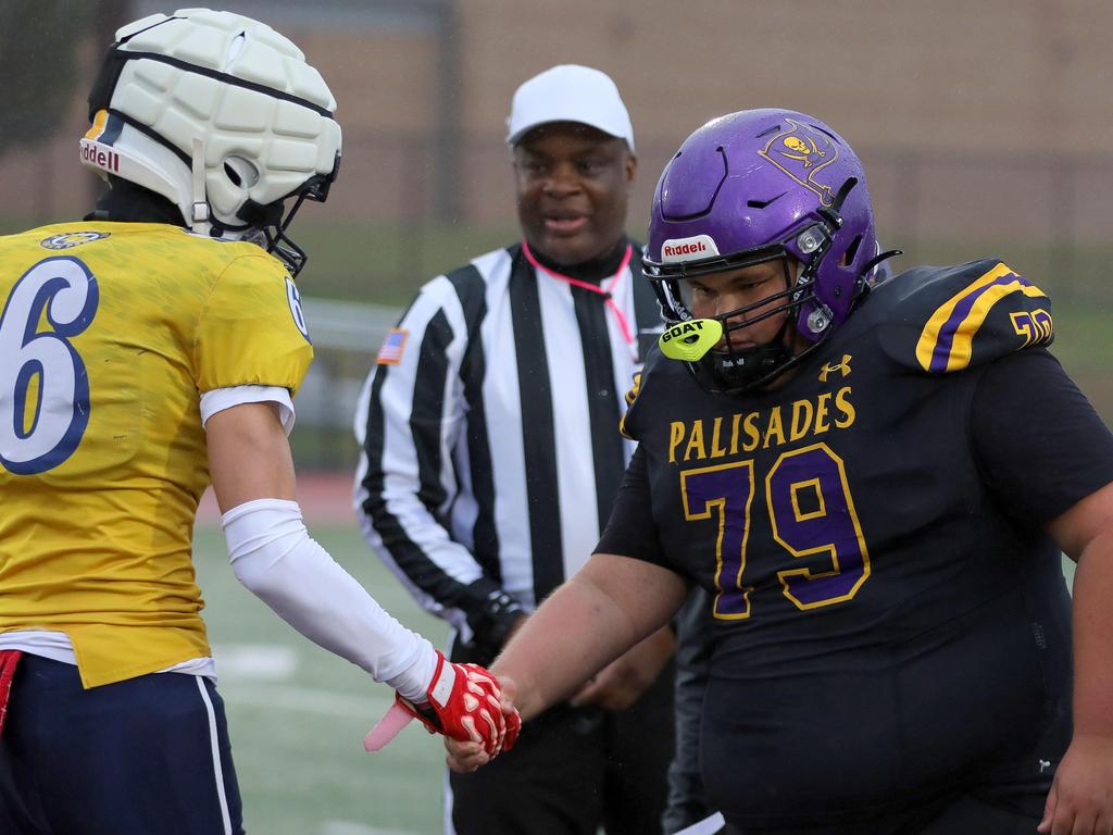 Two football players from opposing teams shake hands in front of a referee.