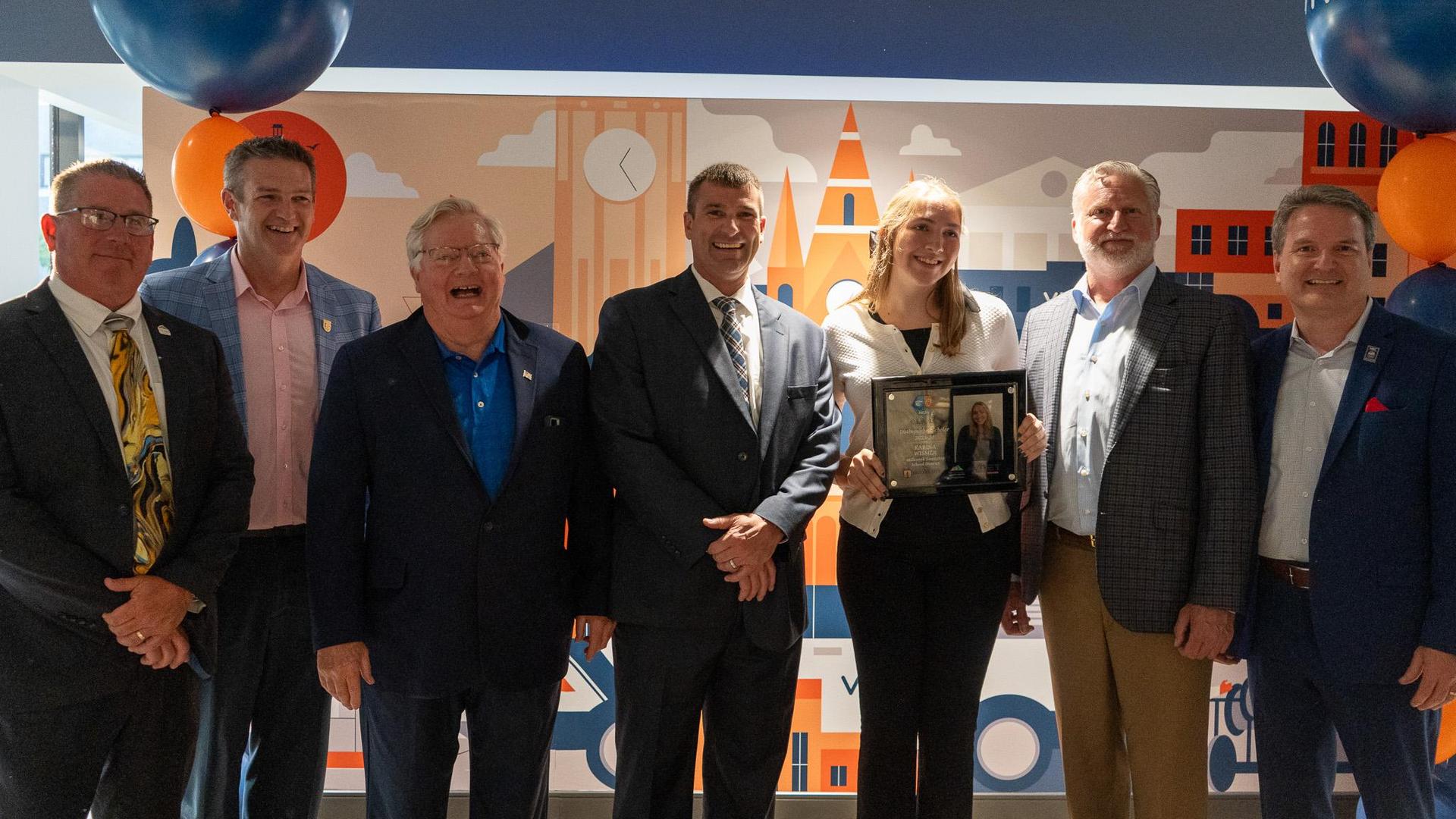Executive Director Brad Whitman poses alongside a student holding an award and scholarship sponsors at a Class Act Scholarship Ceremony.