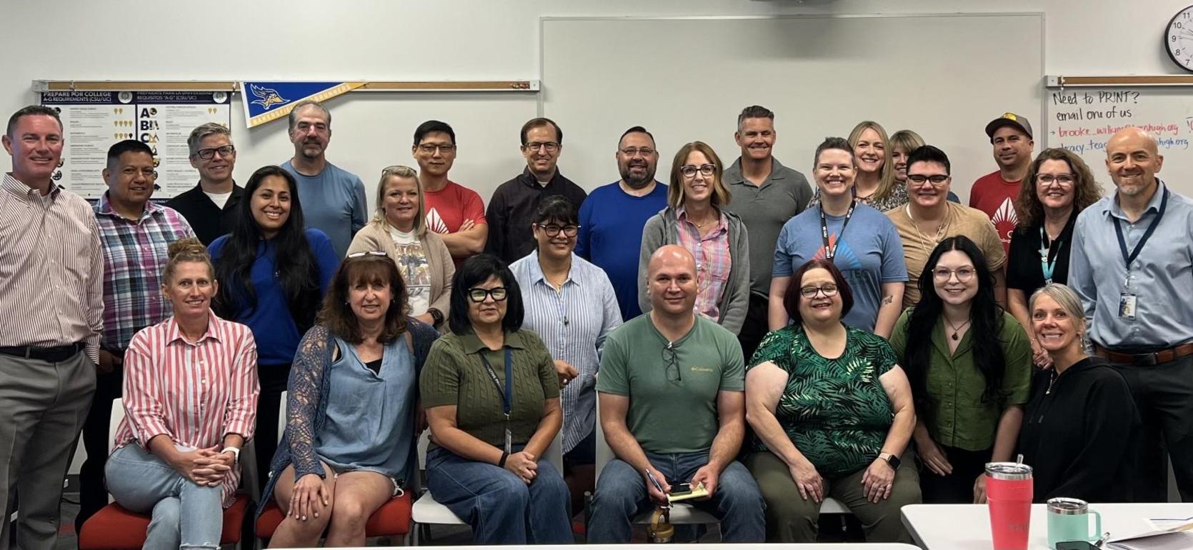 A diverse group of 30 people gathered in a classroom for a photo, smiling and posing.