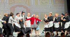 A stage performance featuring a girl in a red sweater surrounded by actors in costumes.