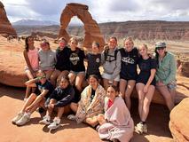 A group of girls poses on red rock formations with a scenic backdrop.