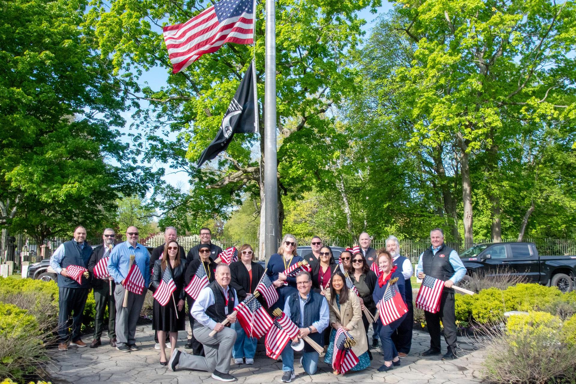 A group poses with American flags and trees in the background.