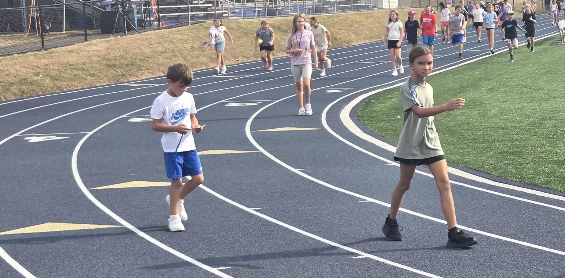 Boy walking and girl alongside a track with a group in the distance.