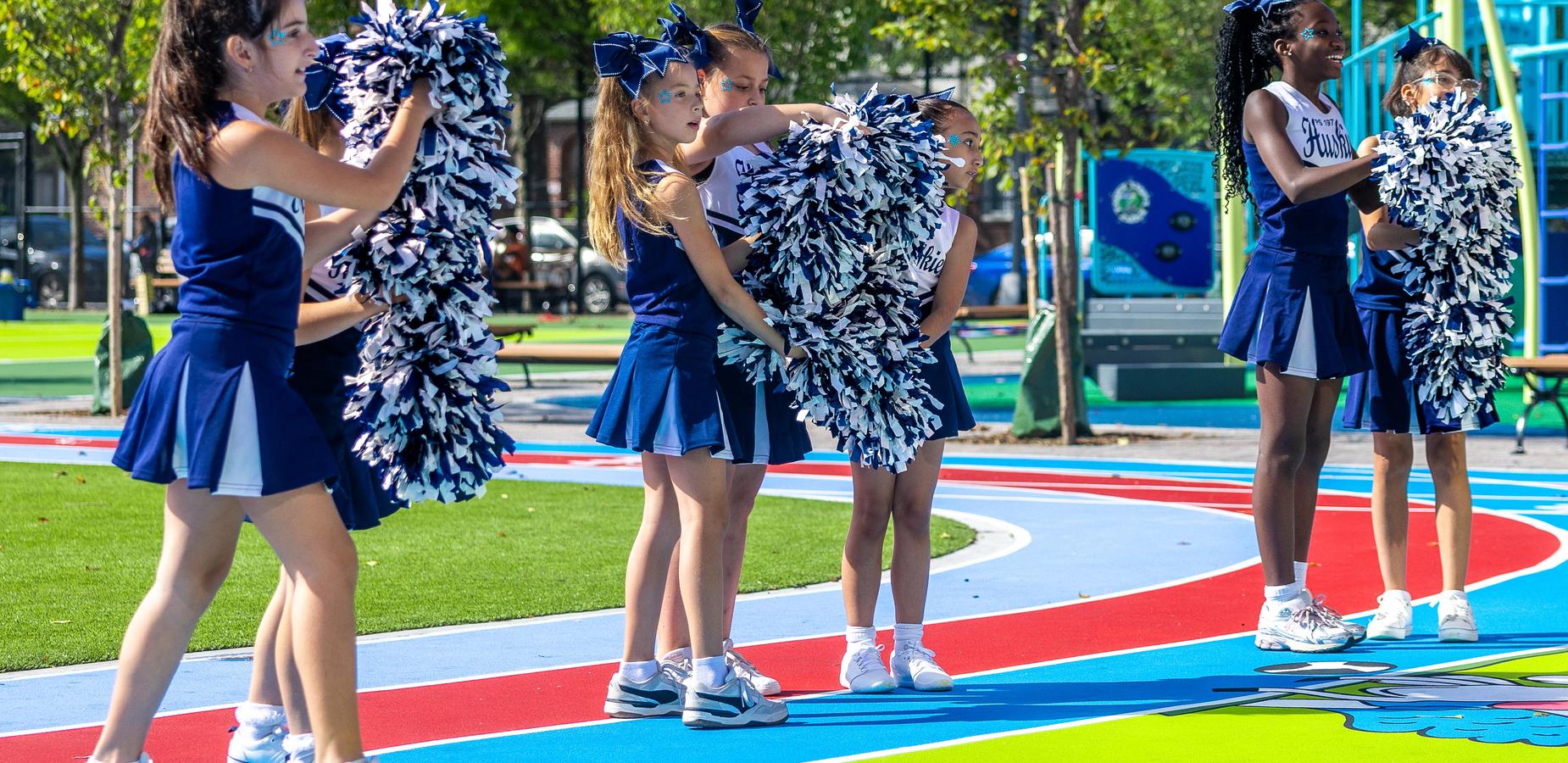 Cheerleaders in uniforms holding pom-poms on a colorful playground.