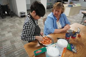 A student gets help spreading out his pizza dough.