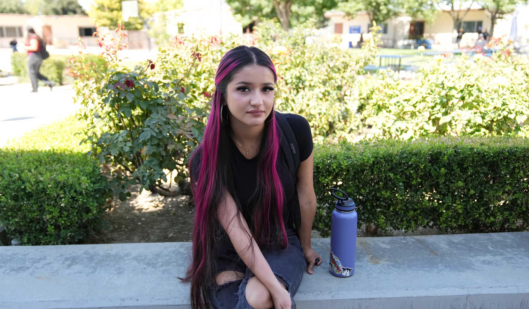 high school girl sitting in front of bushes