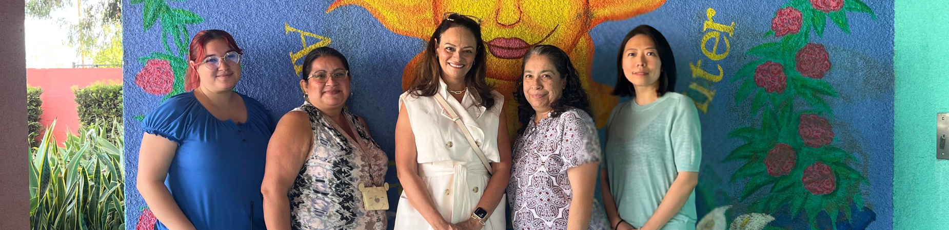 Picture of staff in front of welcome mural