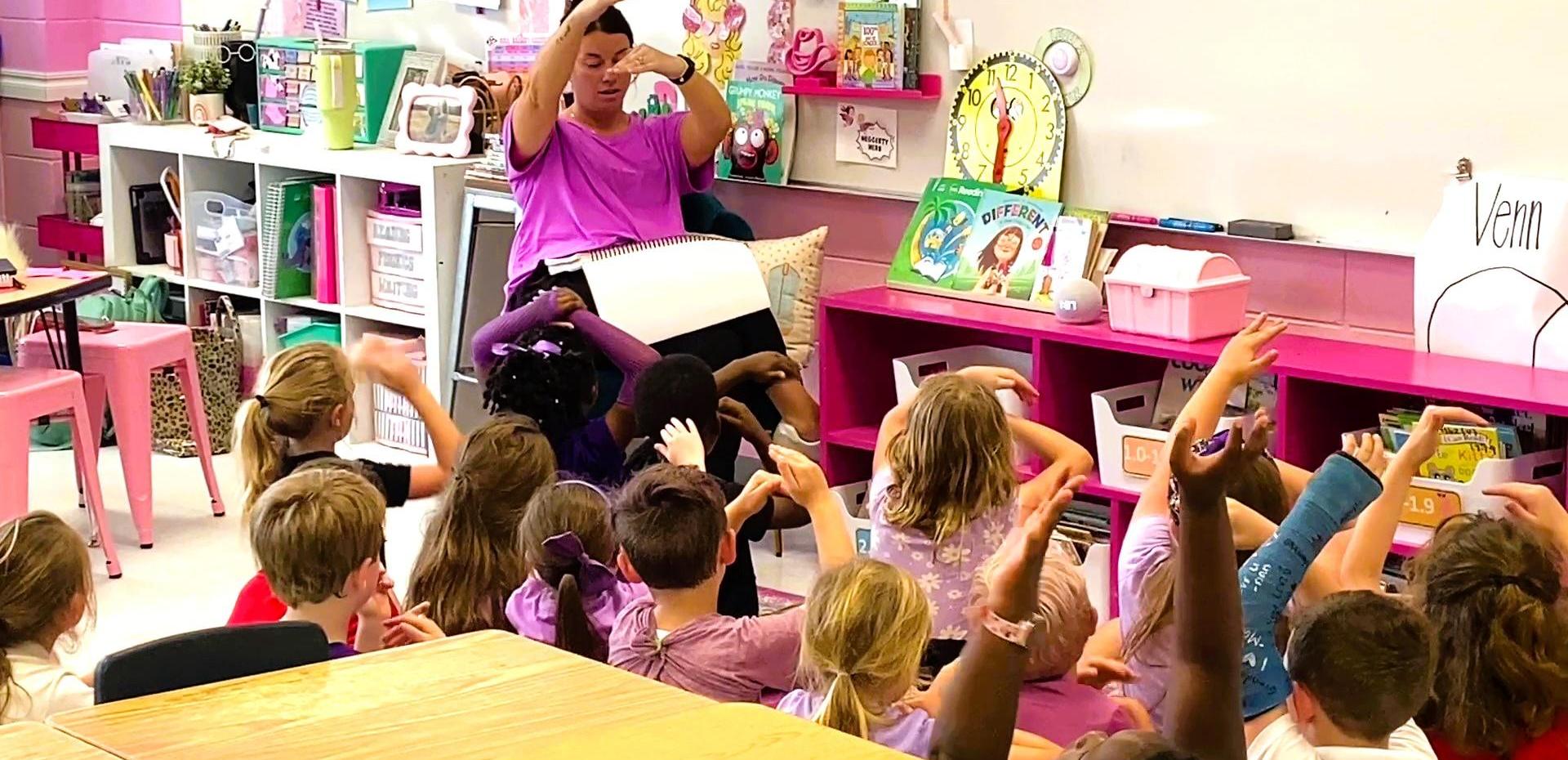 Teacher leading a lesson with young students raising their hands.