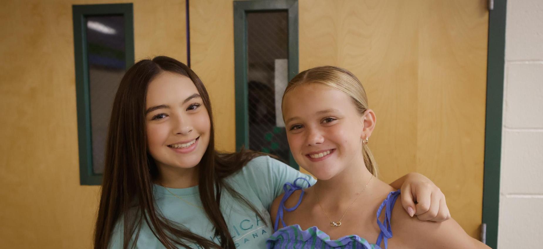 Two girls smiling and posing together in a school hallway.